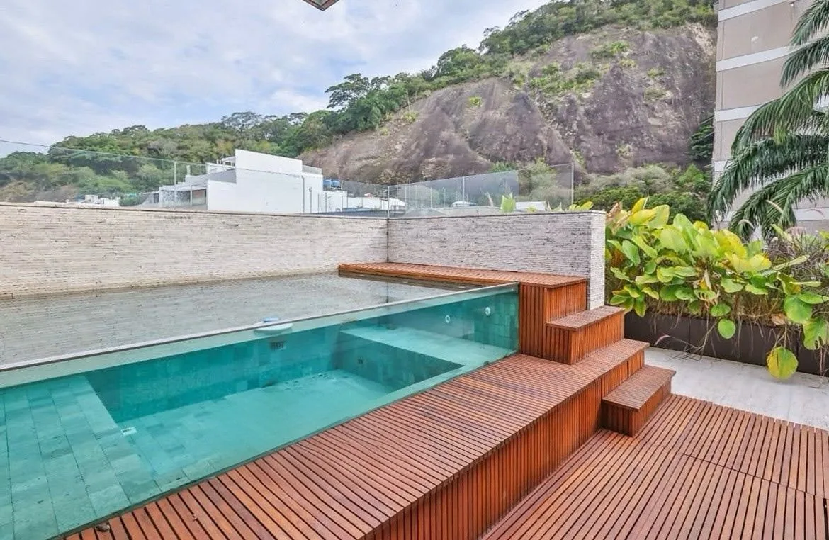 Terraço da cobertura com piscina revestida em pedra, deck de madeira e o morro ao fundo