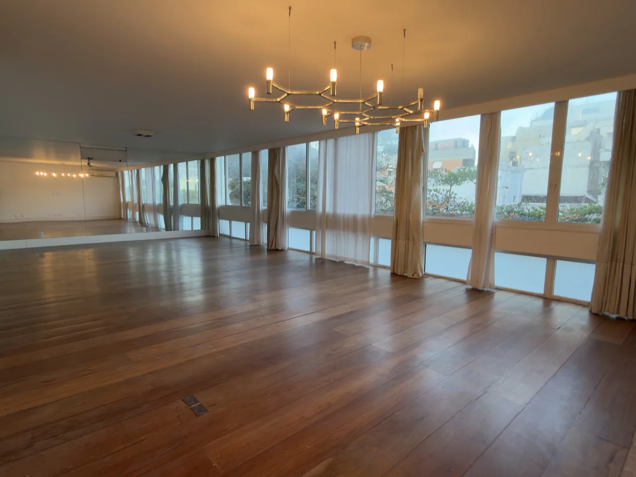 Sala ampla com piso de madeira e janelas panorâmicas