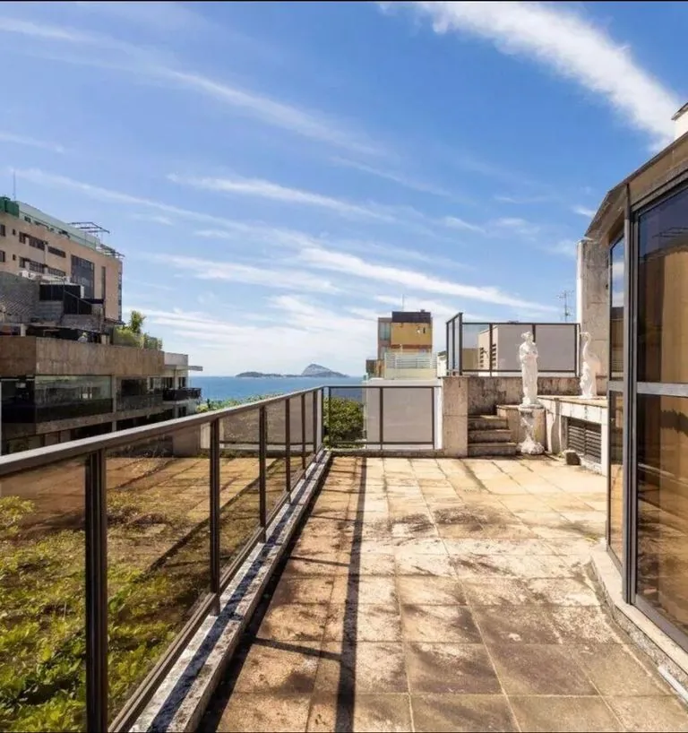 Terraço da cobertura com piso de pedra e vista para o mar do Leblon, com as Ilhas Cagarras ao fundo