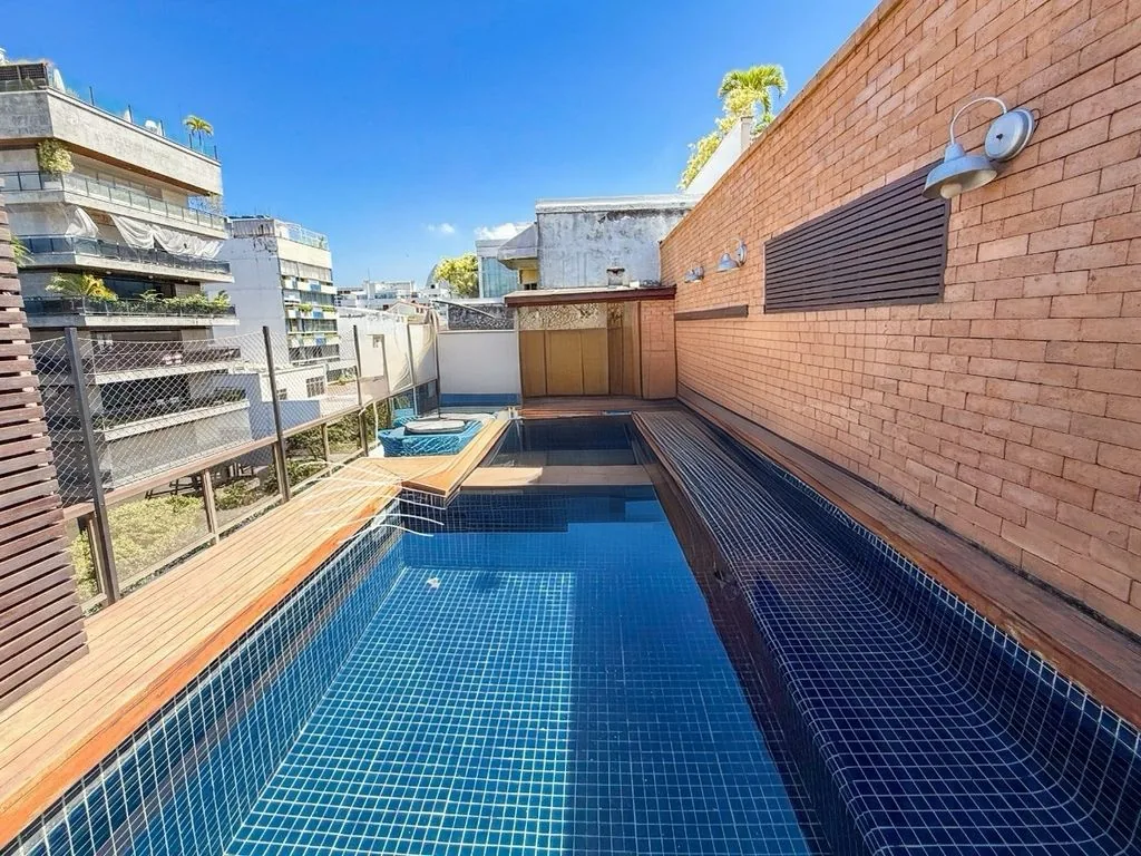 Piscina azulejada com deck de madeira no terraço da cobertura, com os prédios de Ipanema ao redor