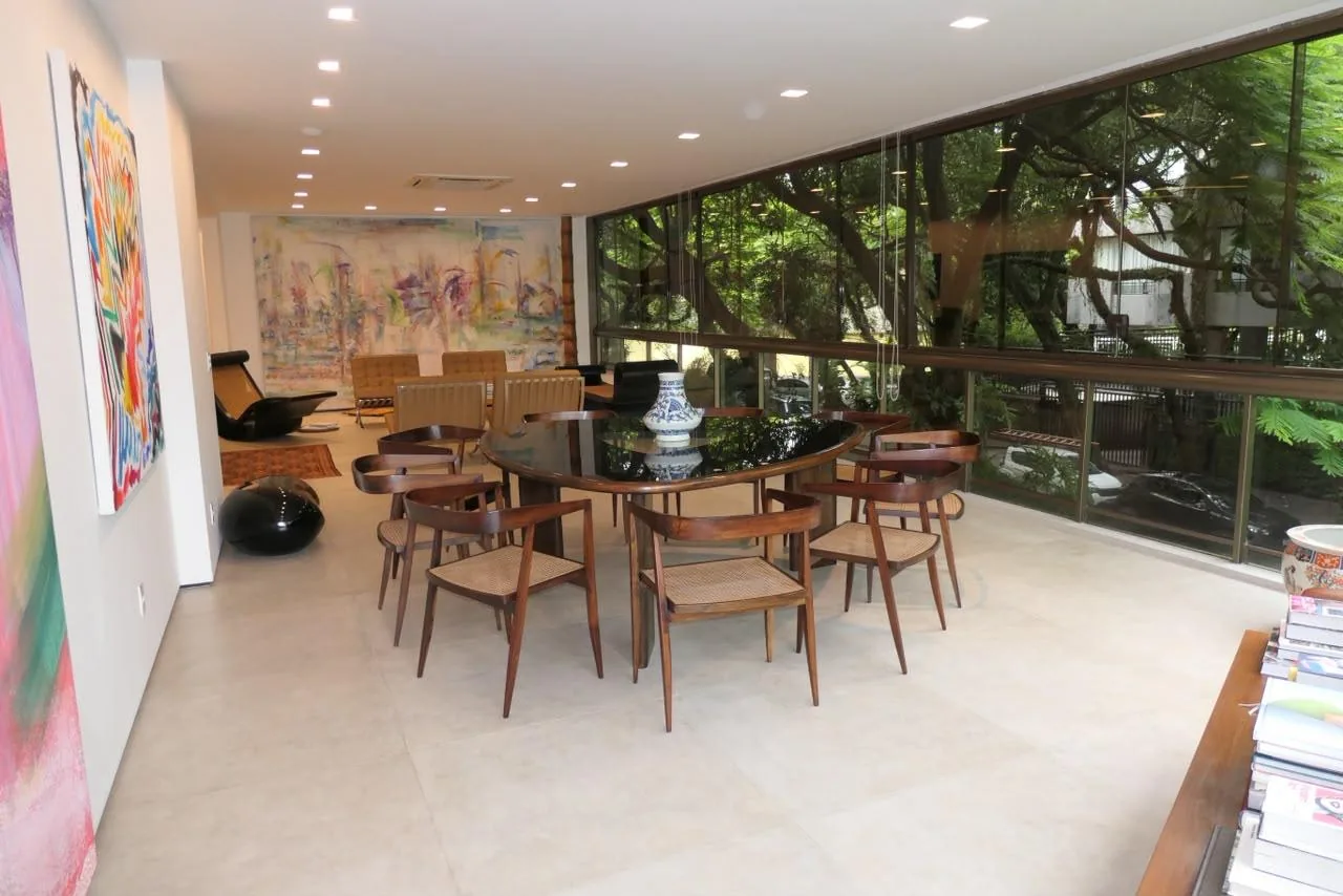 Sala de jantar redonda em madeira escura, cercada de vidro e árvores