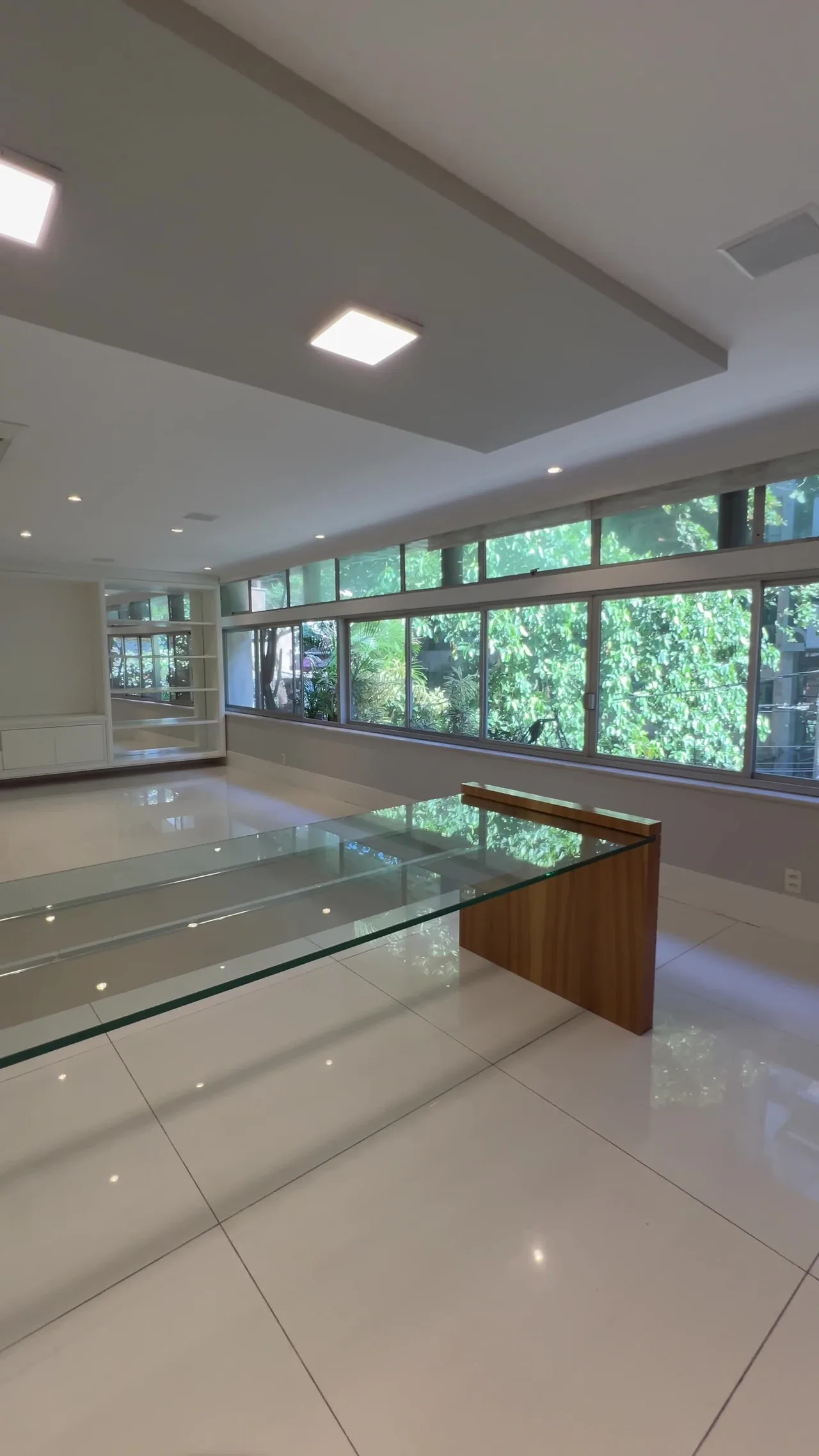 Sala integrada com janelas amplas para o verde e mesa de centro em vidro