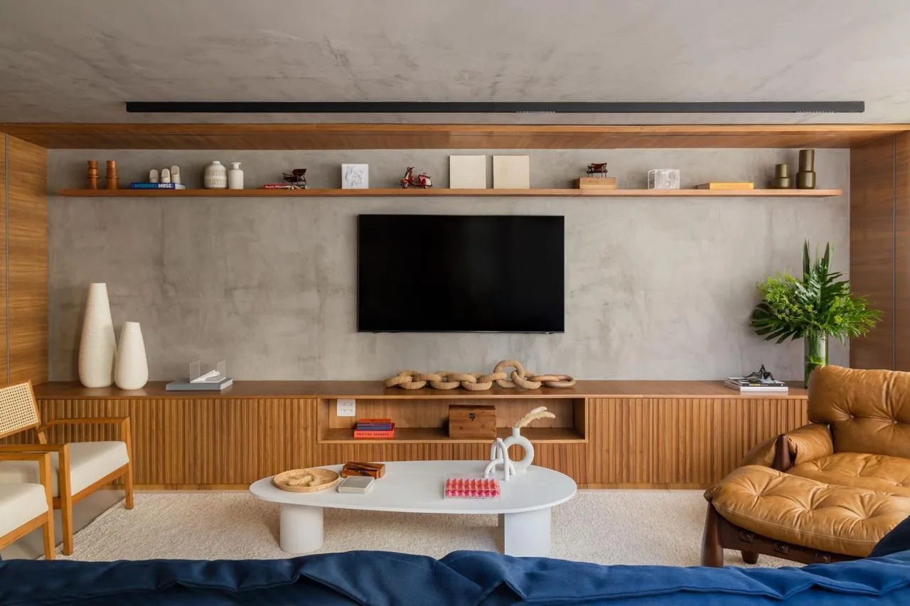 Living com painel de madeira ripada, TV e sofá azul-marinho